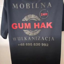 Czarna koszulka z szarym nadrukiem: 'Mobilna GUM HAK Wulkanizacja 24H' i numerem telefonu. Grafika opony. Odzież robocza.