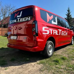 Marta Jankowska M.J StalTech - Czerwony Ford Transit z logo 'MJ STALTECH' na oknach i karoserii, zaparkowany na trawie w słoneczny dzień. Widoczny numer rejestracyjny i elementy nadwozia.