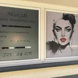 Oklejone folią okno salonu kosmetycznego z grafiką portretu kobiety i informacją o usługach: makijaż permanentny, rzęsy, oczyszczanie wodorowe twarzy i numer telefonu.