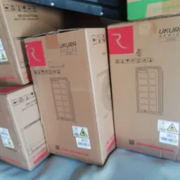 Stos kartonów z klimatyzatorami Ukura Series U35Xo, z widocznymi grafikami i oznaczeniami. Jeden karton częściowo zasłonięty zielonym opakowaniem Kaisai Eco.