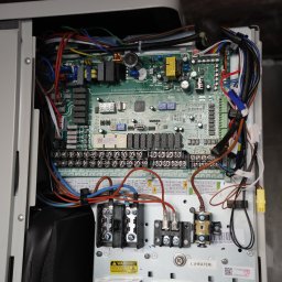 IQDOM 24 - Otwarta obudowa pompy ciepła z widoczną płytą sterującą i okablowaniem.  Widoczne złącza, bezpieczniki i elementy elektroniczne. Górne oświetlenie.