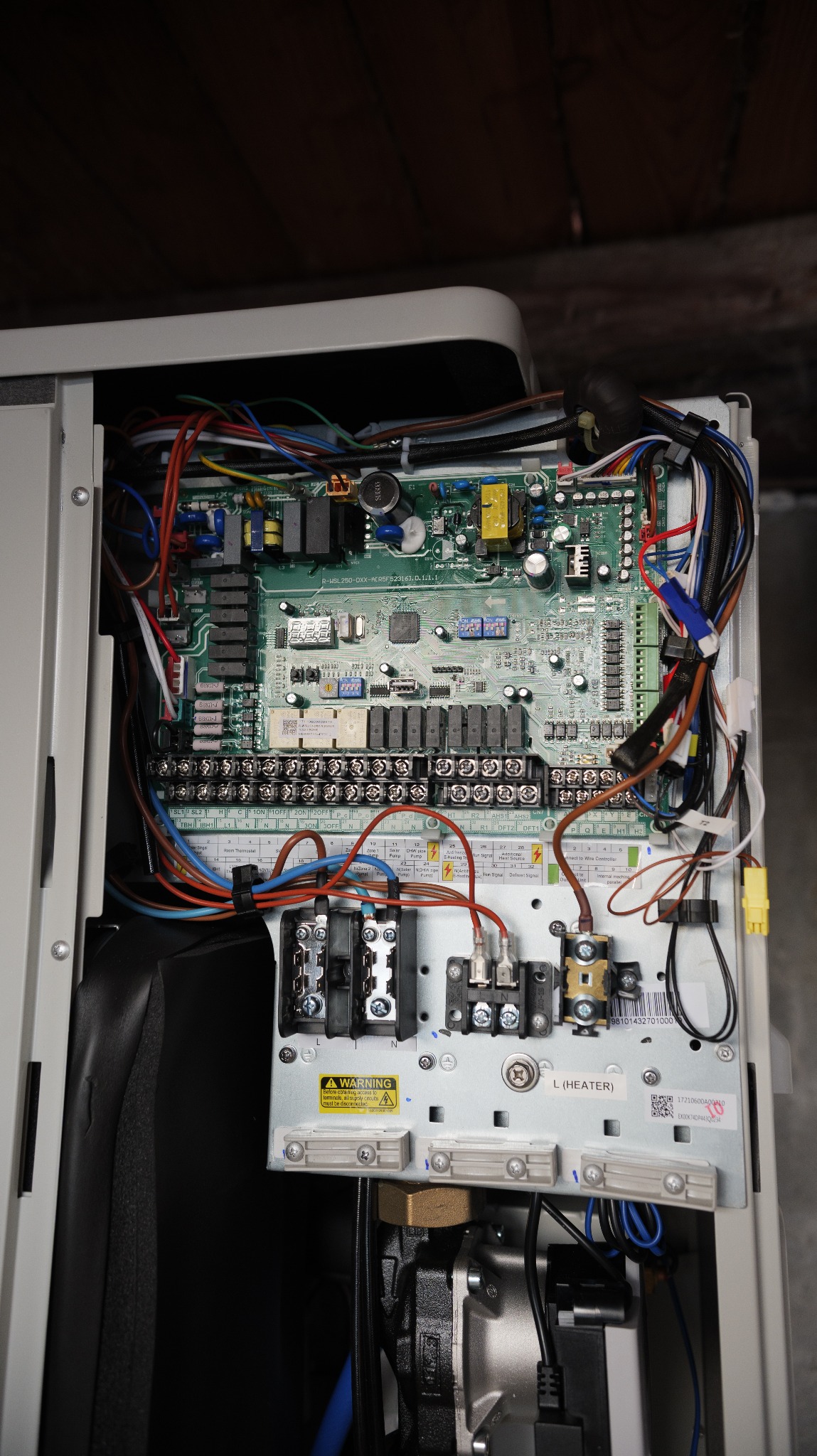 Otwarta obudowa pompy ciepła z widoczną płytą sterującą i okablowaniem.  Widoczne złącza, bezpieczniki i elementy elektroniczne. Górne oświetlenie.