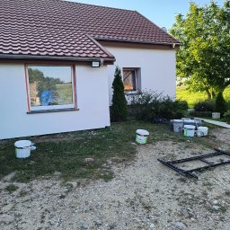 Andrzej Szewczyk usługi remontowo-budowlane - Biała elewacja domu z brązowym dachem po malowaniu, okna zabezpieczone folią. Na pierwszym planie puszki z farbą i rusztowanie.