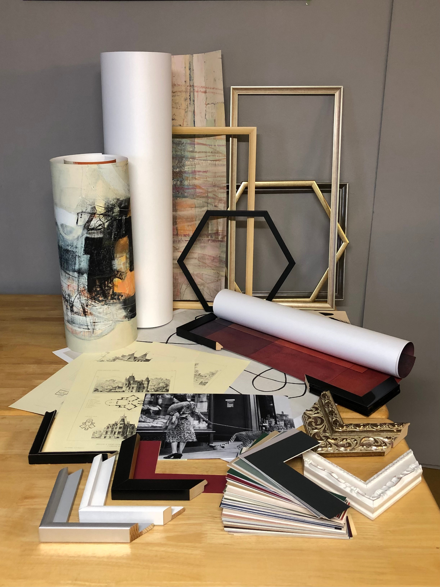 Wzorniki ram, passe-partout i reprodukcje na stole. Widoczne ramy w różnych kształtach i kolorach, zwinięte w rulon projekty i zdjęcia. Prezentacja materiałów do oprawy.