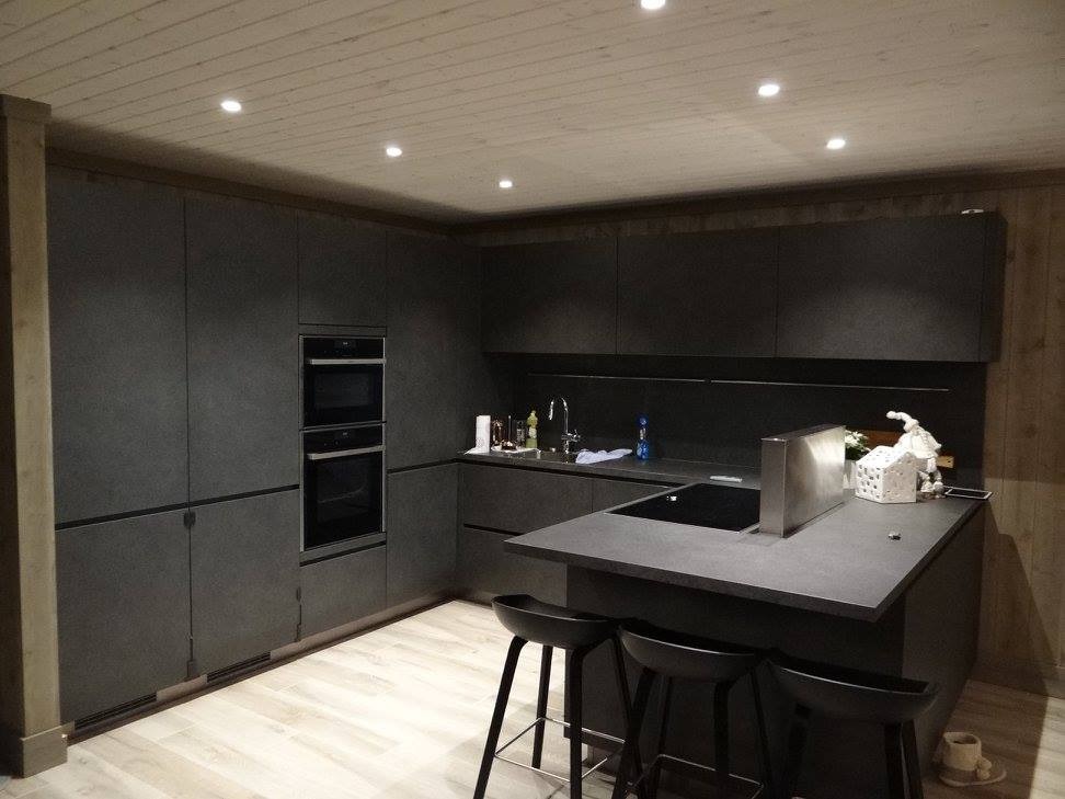 Nowoczesna, minimalistyczna kuchnia w odcieniach szarości z drewnianym sufitem i oświetleniem punktowym. Widoczne wysokie szafki, piekarnik i wyspa z hokerami.