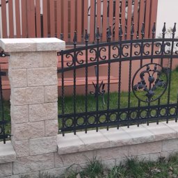Ogrodzenia Kompleks - Czarne, kute ogrodzenie z kamiennymi słupkami i dekoracyjnymi elementami na tle zielonego trawnika i drewnianego płotu.
