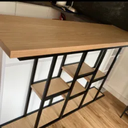 Loftowa konstrukcja: blat z drewna na metalowym stelażu z półkami. Geometryczny design, czarne ramy, jasne drewno. Nowoczesny minimalizm w detalu.