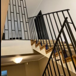 smk.pl Krzysztof Smyczyński - Metalowe schody z czarną balustradą i poręczą w domu w Toruniu. Nowoczesny design z pionowymi szczeblami. Widok z dołu, oświetlenie sufitowe.