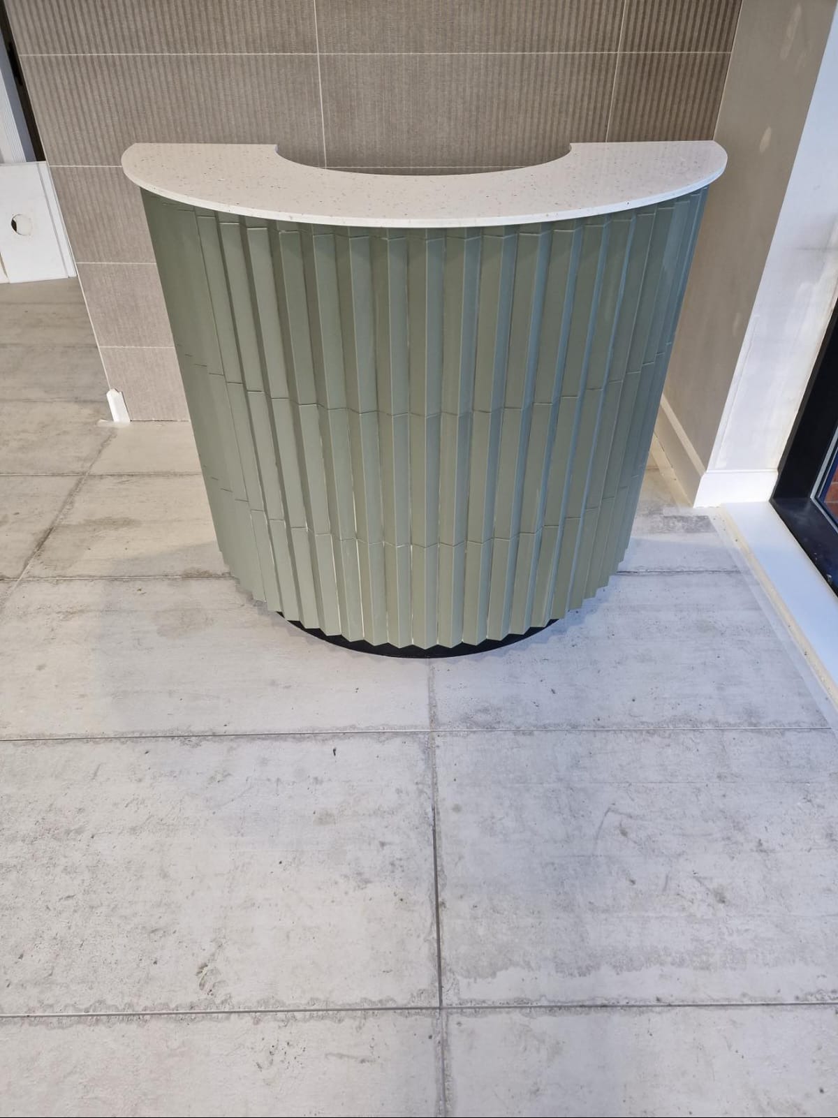 Wykończona, półokrągła lada z zielonymi płytkami i białym blatem, na tle płytek ściennych i podłogowych. Widok z góry ukazuje detale wykończenia.