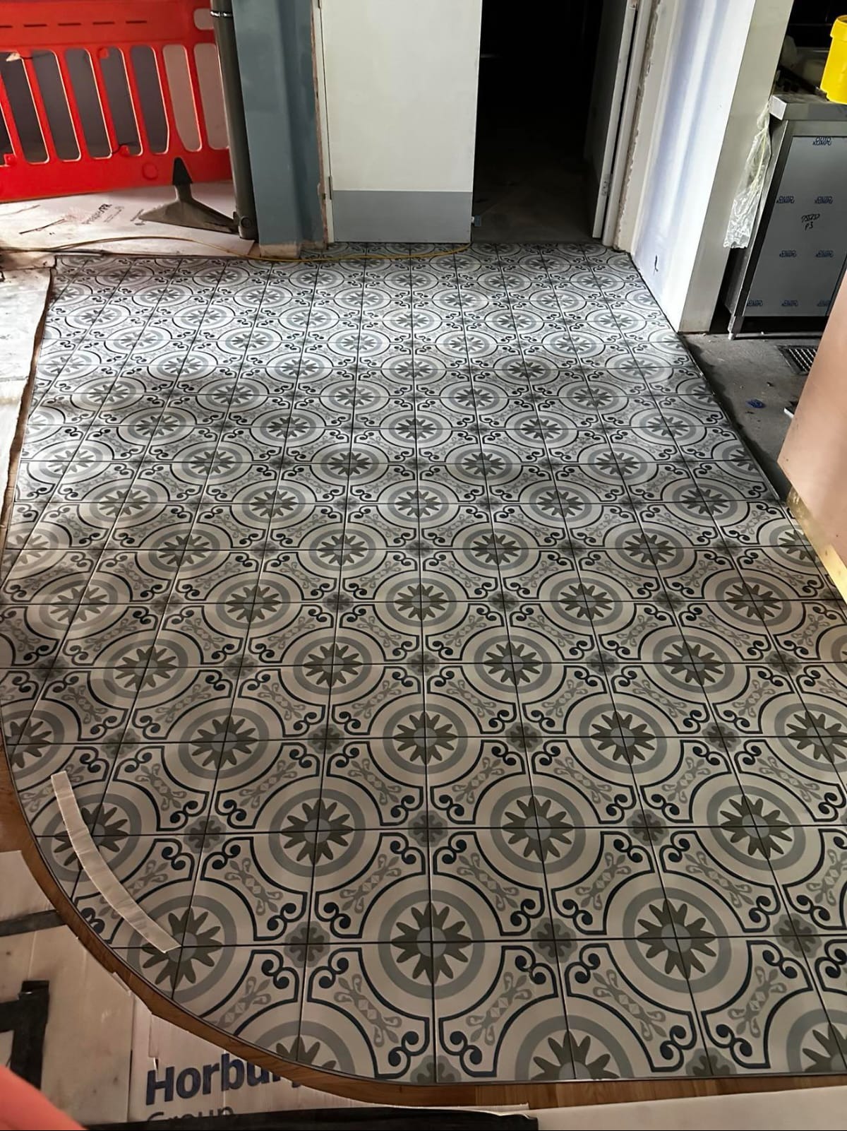 Ułożona podłoga z szarych płytek w geometryczny wzór, widok z góry, częściowo zakryta kartonami. Wykończenie podłogi w stylu retro.