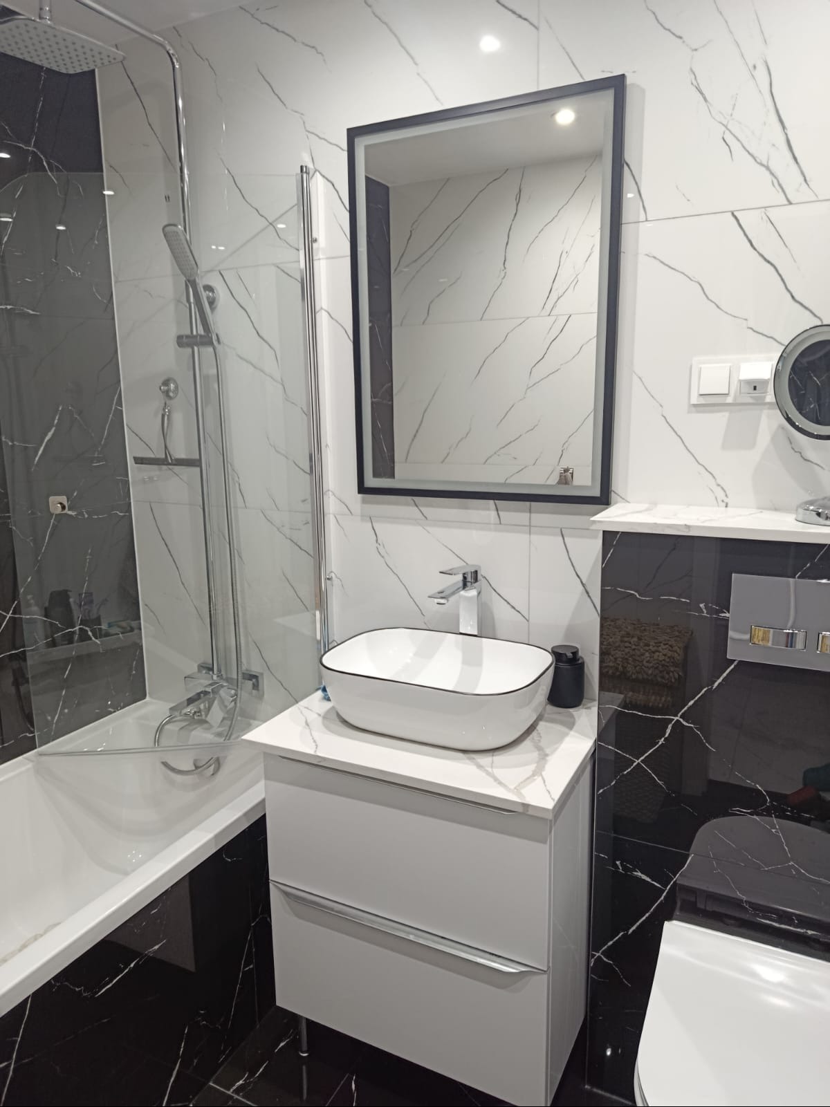 Nowoczesna łazienka z wanną, umywalką nablatową i lustrem w czarnej ramie. Biało-czarne marmurowe płytki na ścianach i podłodze.