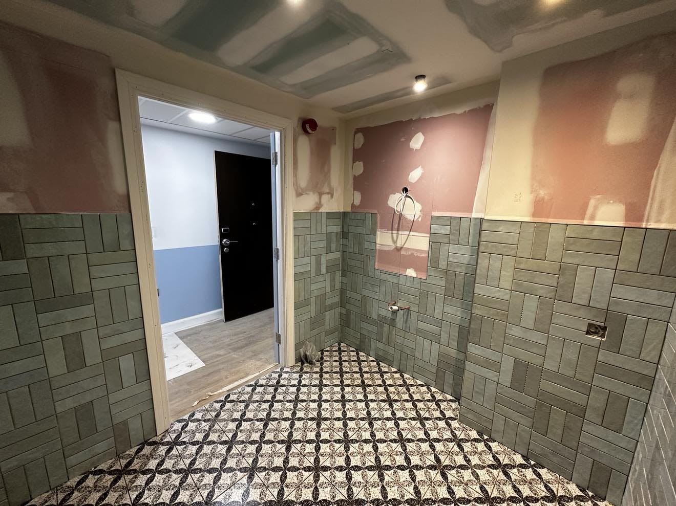 Łazienka w trakcie remontu: ułożona podłoga z wzorem, częściowo wyłożone ściany zieloną glazurą w układzie cegiełki, sufit przygotowany do malowania.