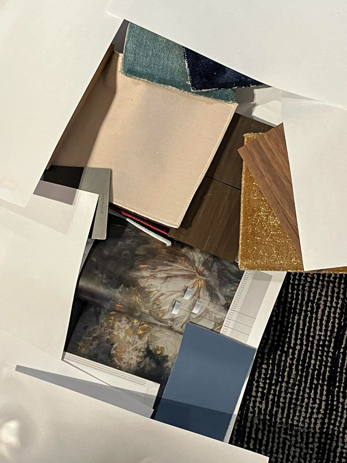 Moodboard z próbkami materiałów wykończeniowych: tkaniny, drewno, farby. Elementy ułożone warstwowo w białym pudełku, ukazujące różnorodność faktur i kolorów.