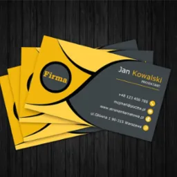 Stos wizytówek w odcieniach żółci i szarości na ciemnym tle imitującym drewno. Wizytówka z imieniem Jan Kowalski i danymi kontaktowymi.
