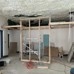 Thermobud Sp. z o.o. - Poddasze w trakcie ocieplania pianą PUR, widoczne rusztowanie i materiały budowlane. Na suficie nierównomierna warstwa piany. Prace wykończeniowe wewnątrz budynku.