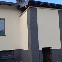 Thermobud Sp. z o.o. - Dwukolorowa elewacja domu jednorodzinnego, z elementami w odcieniach szarości i jasnego beżu, widok z zewnątrz, częściowo widoczny pracownik w trakcie pracy.