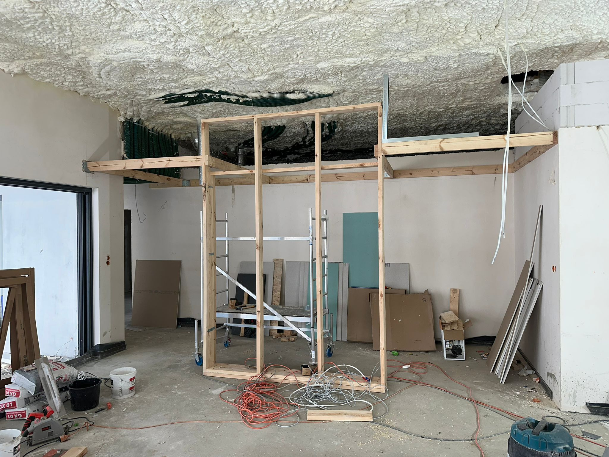 Poddasze w trakcie ocieplania pianą PUR, widoczne rusztowanie i materiały budowlane. Na suficie nierównomierna warstwa piany. Prace wykończeniowe wewnątrz budynku.