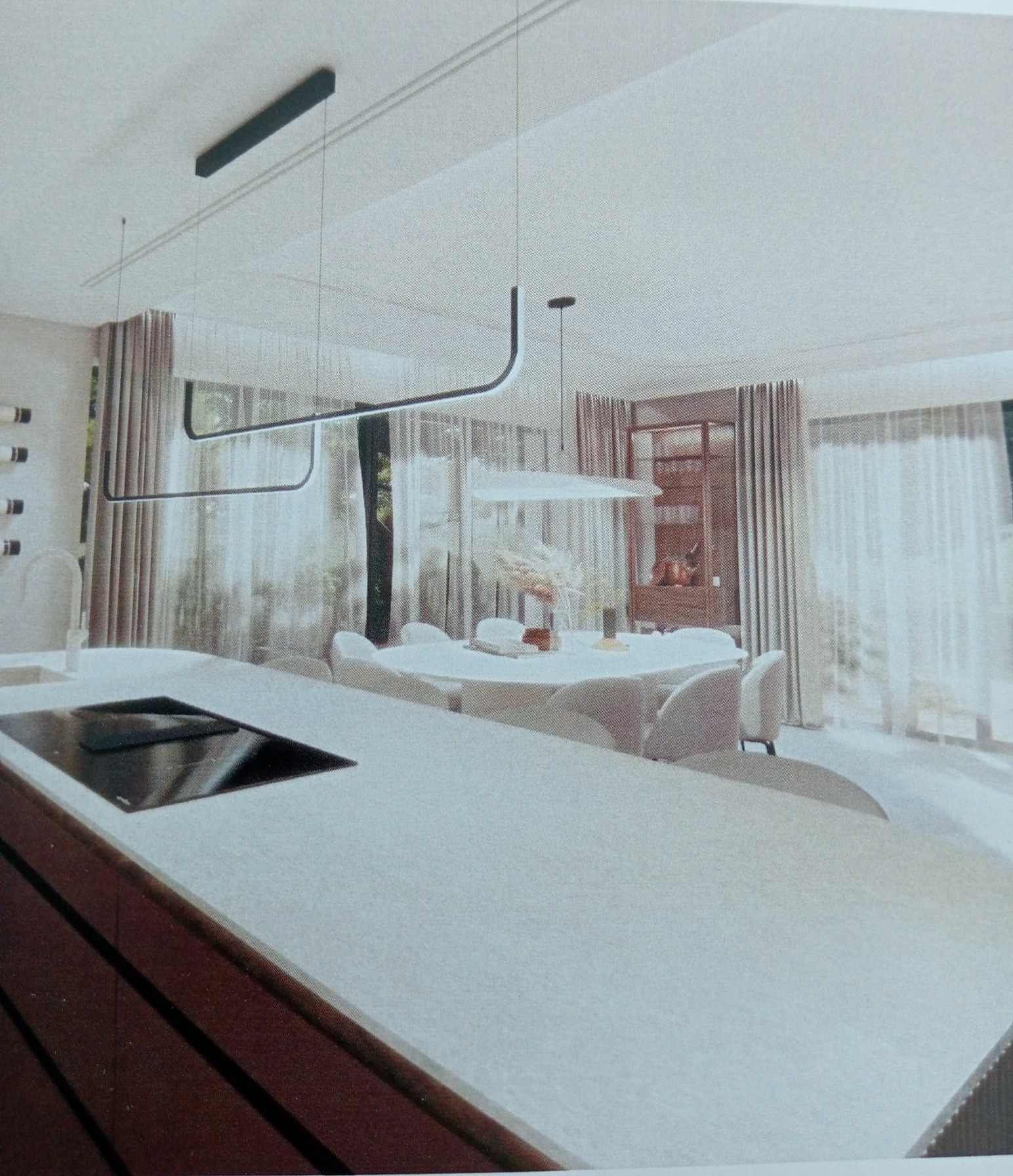 Minimalistyczna kuchnia z wyspą i jadalnią w tle, oświetlona nowoczesnymi lampami wiszącymi. Projekt wnętrza w Gdańsku.