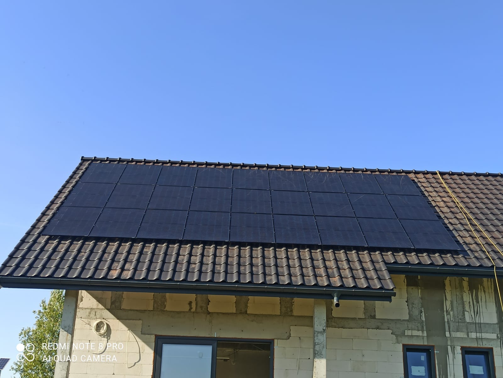 Panele słoneczne na brązowym dachu domu w trakcie budowy, błękitne niebo w tle. Widoczny kabel na dachu. Ujęcie z dołu.