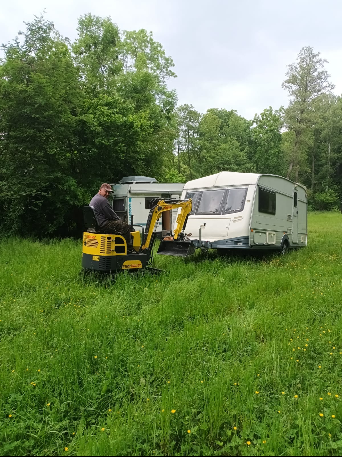 Operator na mini koparce Interbauer w Świebodzinie, na tle przyczep kempingowych i zieleni. Prace ziemne w toku. Specjalistyczny sprzęt.