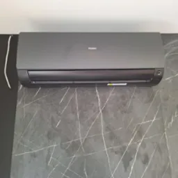 Szary klimatyzator Haier na ścianie z szarego marmuru z białymi żyłami. Widoczny biały kabel. Nowoczesne wnętrze.