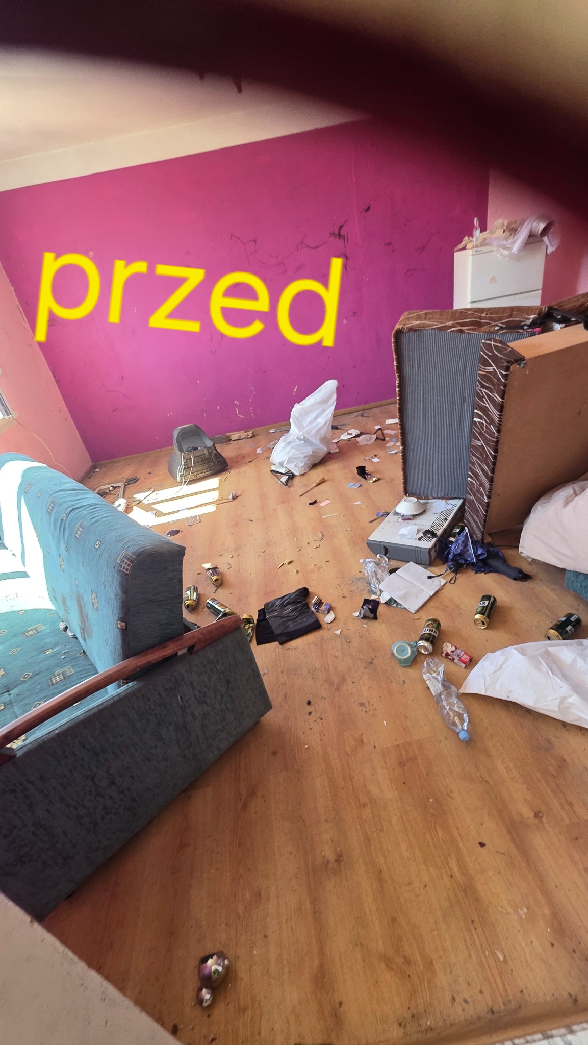Zdjęcie pokoju przed opróżnianiem: widoczny bałagan, porozrzucane przedmioty, puszki po napojach, resztki jedzenia i meble w nieładzie. Na ścianie napis 'przed'.
