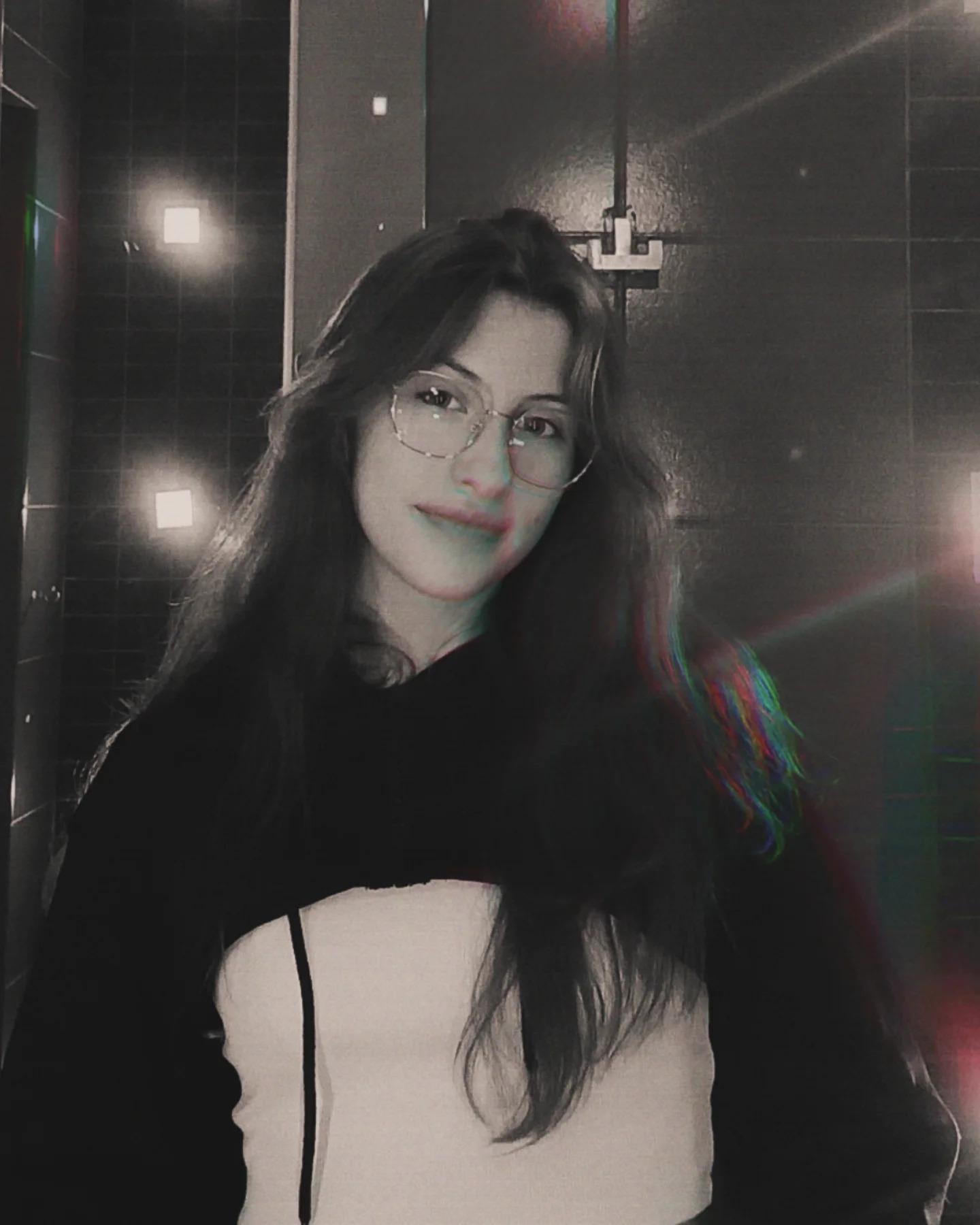 Portret kobiety w okularach na tle czarno-białej ściany z oświetleniem. Efekt glitch art dodaje unikalnego charakteru.