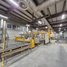 LEDINSIDE INVEST SPÓŁKA Z OGRANICZONĄ ODPOWIEDZIALNOŚCIĄ - Wnętrze hali produkcyjnej z systemem oświetlenia jarzeniowego zamontowanym pod sufitem, widoczne instalacje wentylacyjne i maszyny produkcyjne.