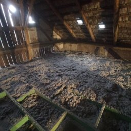 RPGO SPÓŁKA Z OGRANICZONĄ ODPOWIEDZIALNOŚCIĄ - Poddasze z widoczną warstwą izolacji termicznej, włóknista struktura materiału wypełnia przestrzeń między elementami drewnianej konstrukcji dachu. Widoczne okna dachowe.