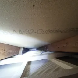 Skośny widok na izolację poddasza z widoczną konstrukcją drewnianą i napisem 'A-32-Outside-UP'.