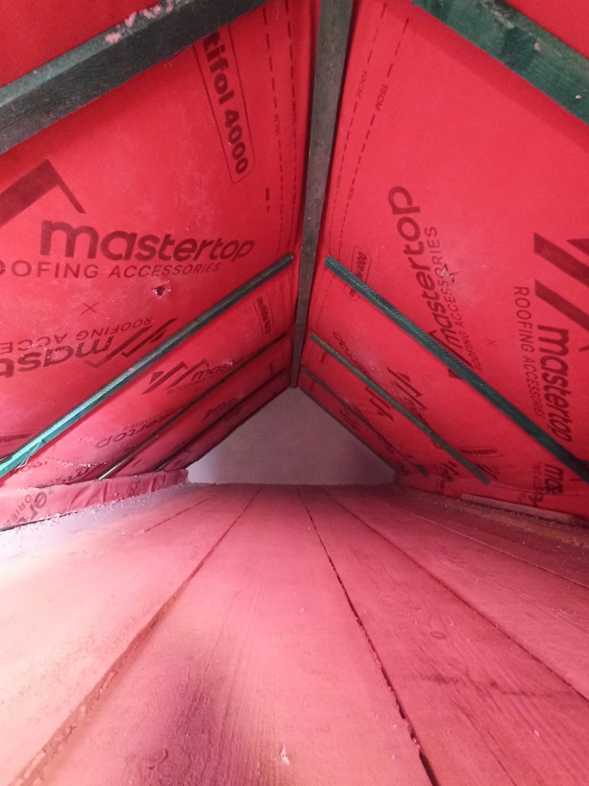 Ocieplenie poddasza wełną mineralną, widok od wewnątrz. Czerwona folia paroizolacyjna Mastertop i drewniana konstrukcja dachu. Izolacja na podłodze poddasza.