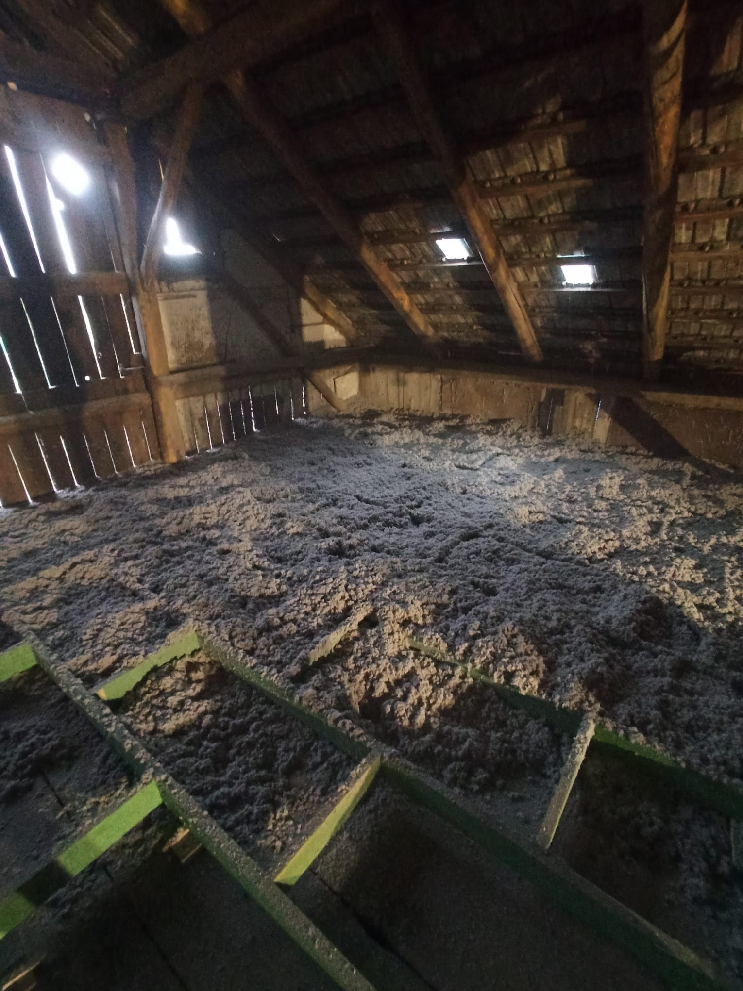 Poddasze z widoczną warstwą izolacji termicznej, włóknista struktura materiału wypełnia przestrzeń między elementami drewnianej konstrukcji dachu. Widoczne okna dachowe.