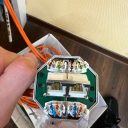 Klimczyk-Elektro - Złącze kablowe w dłoni, widoczne kable w różnych kolorach podłączone do modułu. Element instalacji sieciowej, instalacja domowa, kable pomarańczowe.