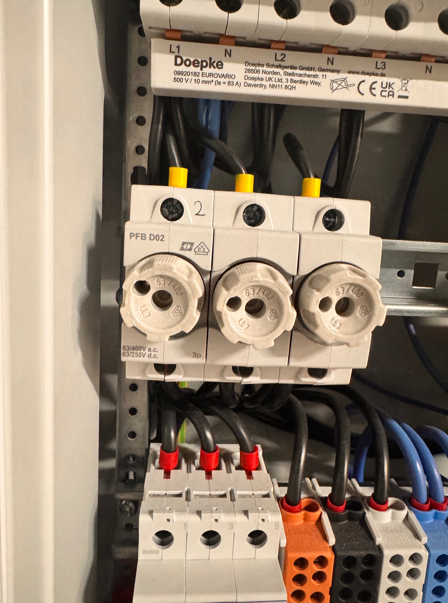 Rozdzielnica elektryczna Doepke z bezpiecznikami topikowymi 63/400, widoczne kable w czarnych peszlach z żółtymi, czerwonymi i pomarańczowymi końcówkami.