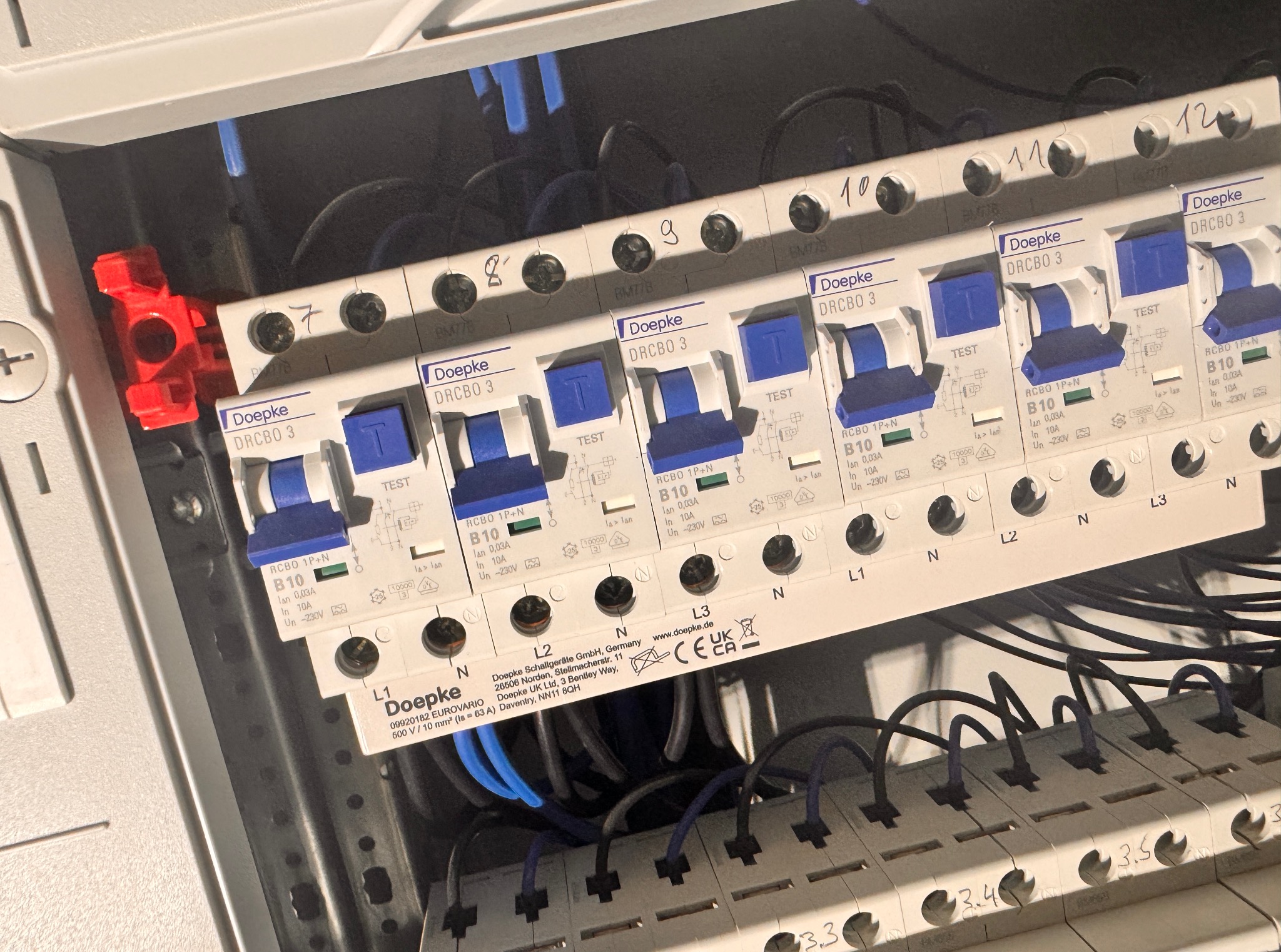 Rozdzielnica elektryczna z zainstalowanymi bezpiecznikami Doepke DRCBO 3. Widoczne przewody i oznaczenia L1, L2, L3, N oraz numery bezpieczników od 7 do 12.