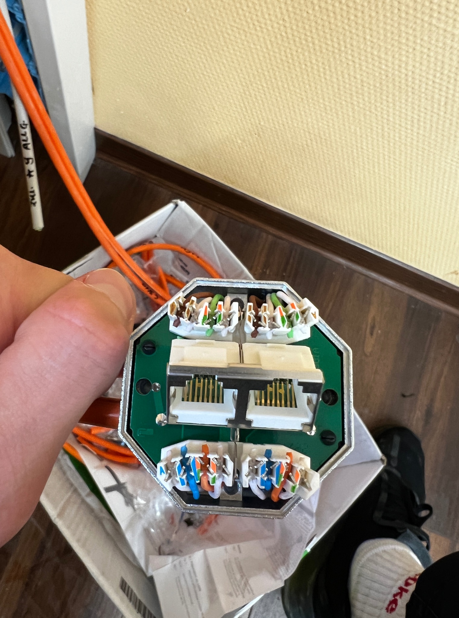 Złącze kablowe w dłoni, widoczne kable w różnych kolorach podłączone do modułu. Element instalacji sieciowej, instalacja domowa, kable pomarańczowe.