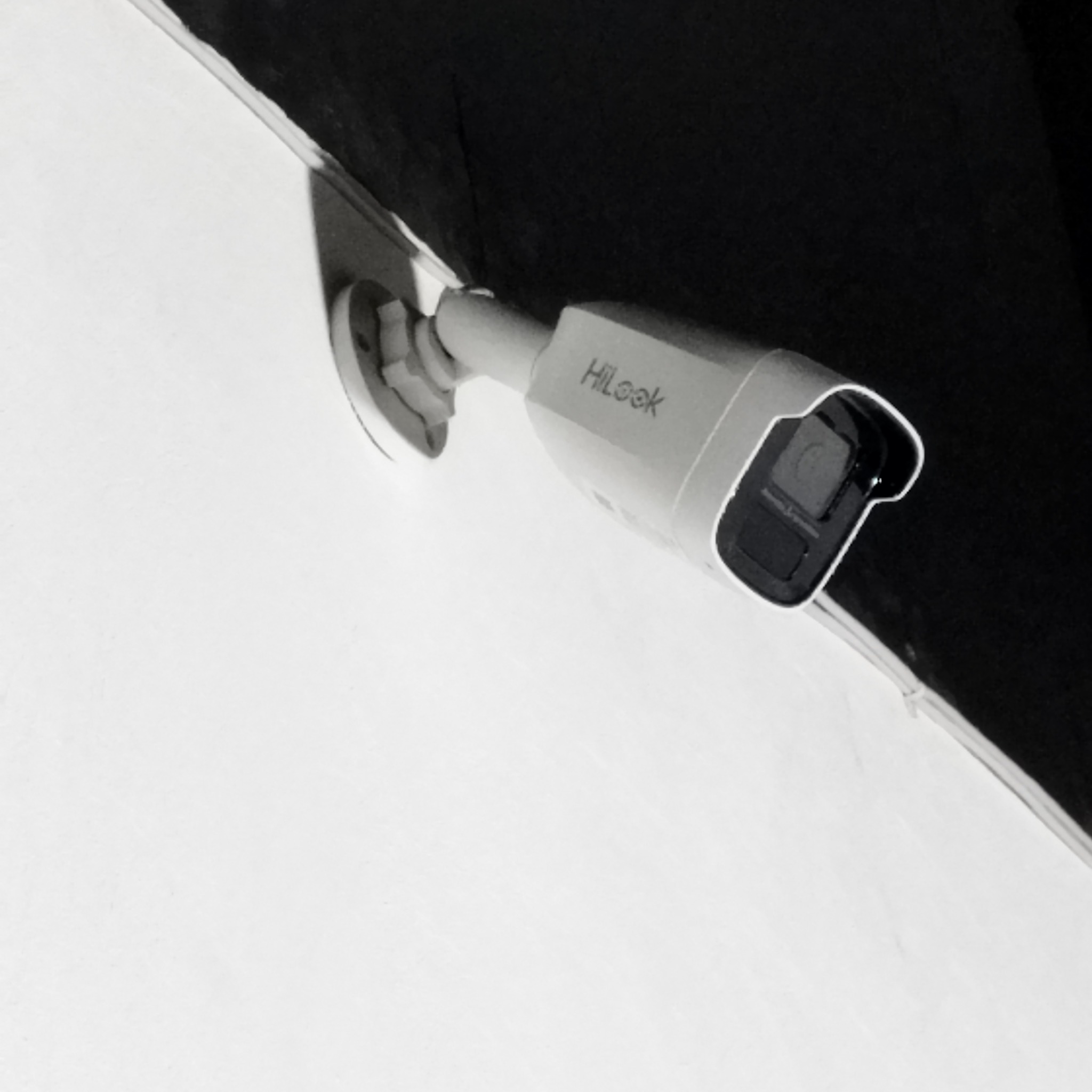 Kamera HiLook zamontowana na białej ścianie pod ciemnym sufitem, widok z dołu pod kątem.