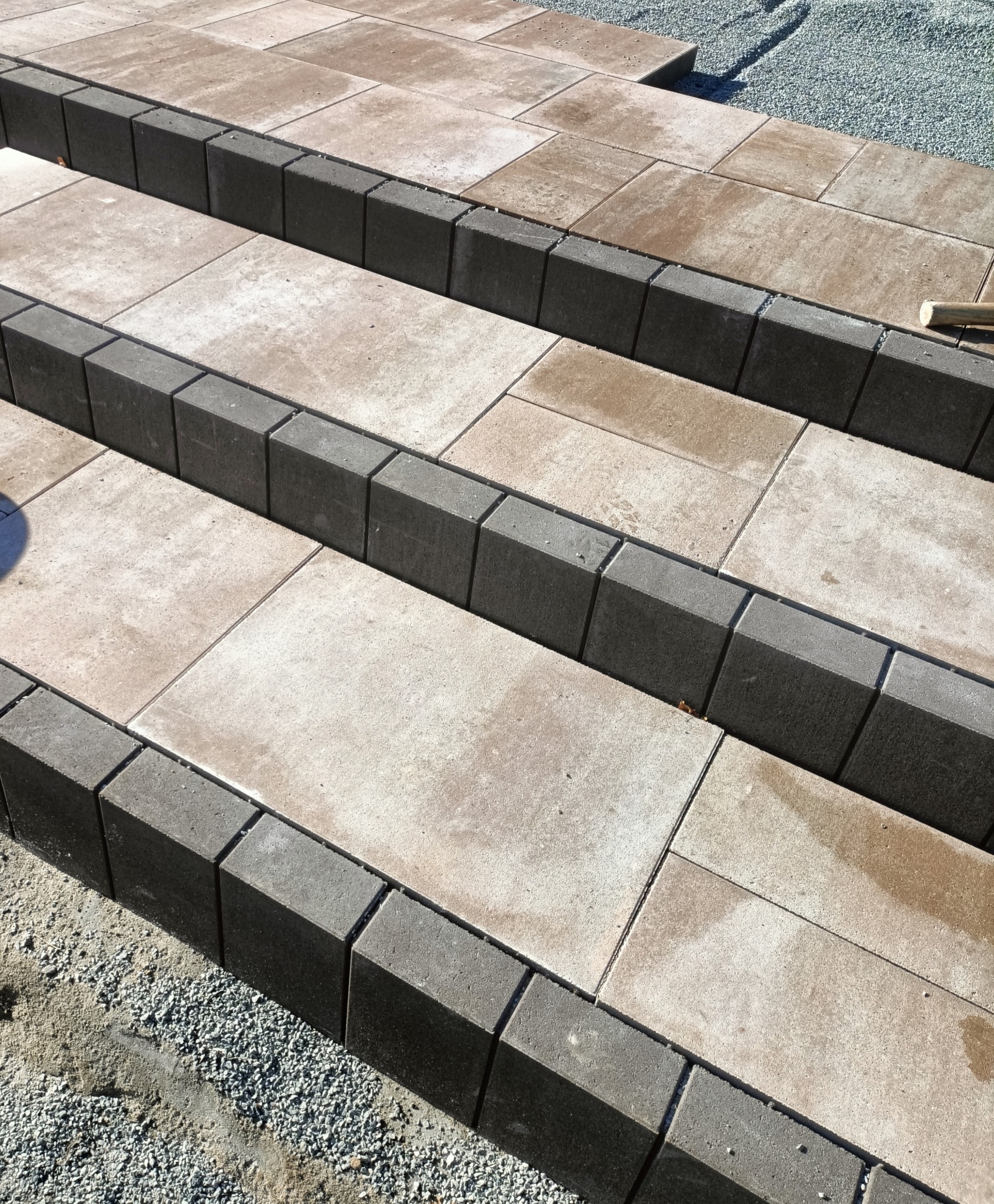 Schody z kostki brukowej w trakcie budowy, z widocznymi obrzeżami i podsypką żwirową. Ujęcie z góry, ukazujące detale i fakturę materiałów.