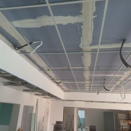 NK ProBud Usługi Ogólnobudowlane Nikodem Kostuch - Sufit z płyt gipsowo-kartonowych w trakcie montażu, widoczne profile i częściowo zaszpachlowane łączenia. Prace wykończeniowe w nowym wnętrzu.