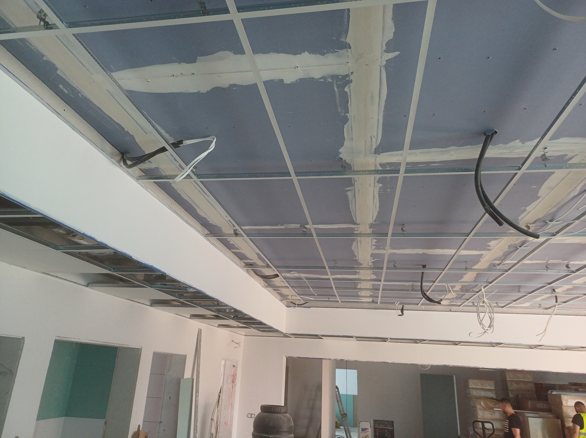 Sufit z płyt gipsowo-kartonowych w trakcie montażu, widoczne profile i częściowo zaszpachlowane łączenia. Prace wykończeniowe w nowym wnętrzu.