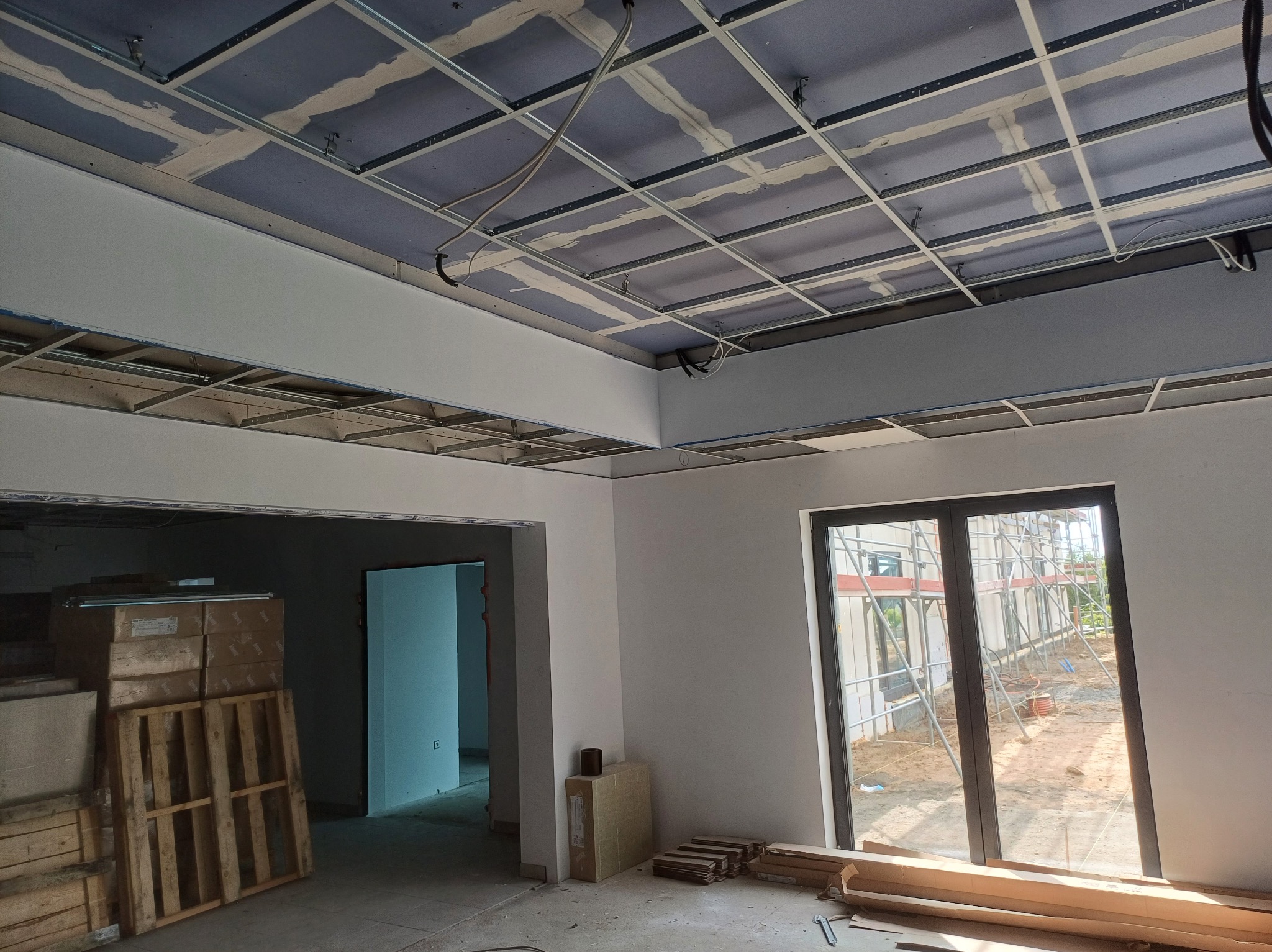 Montaż sufitu podwieszanego z płyt gipsowych w Mirachowie. Widoczne profile i płyty przed szpachlowaniem. Częściowo wykończone ściany, okno i materiały budowlane.