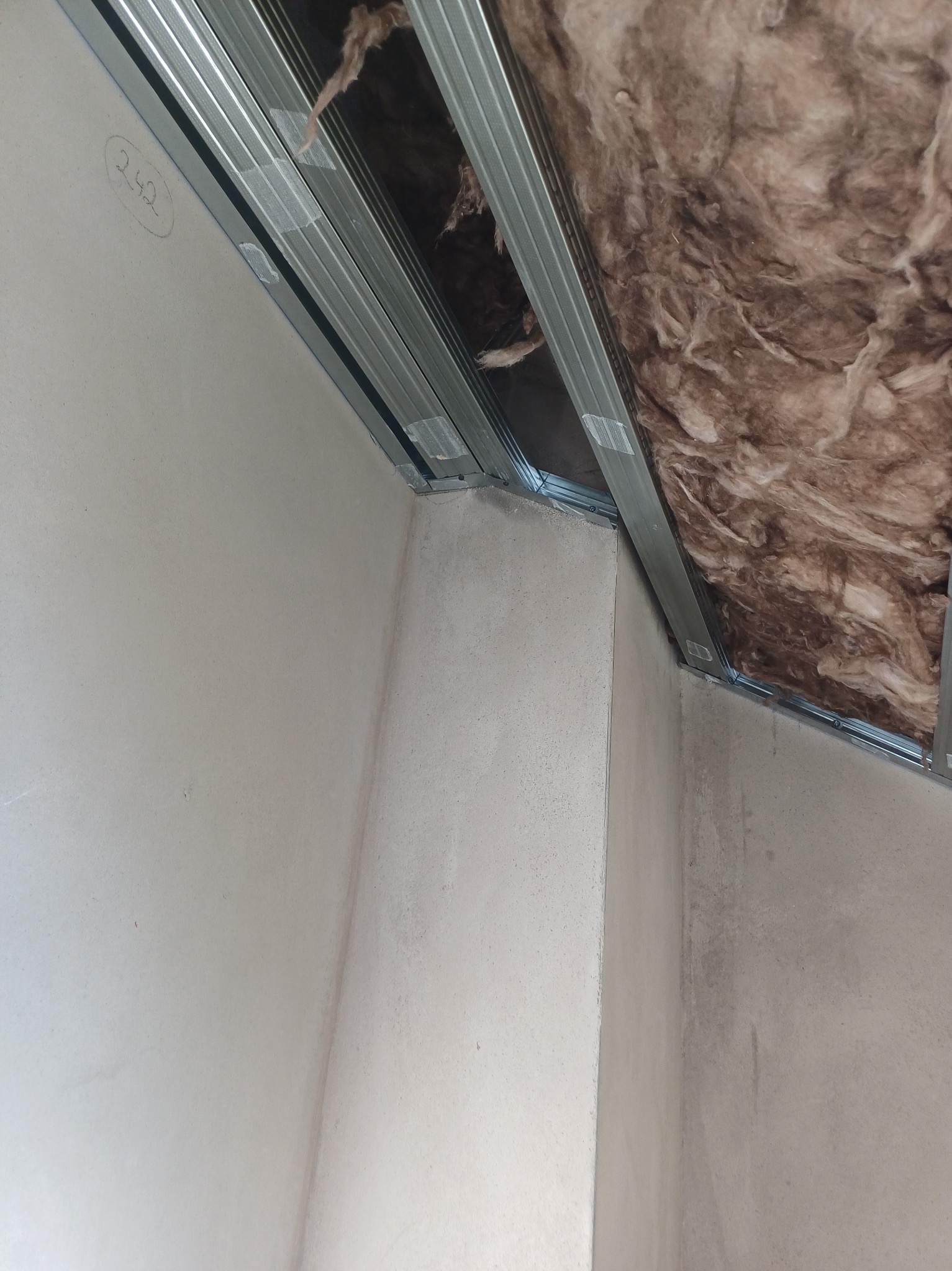 Montaż sufitu podwieszanego: metalowa konstrukcja z izolacją z wełny mineralnej, przytwierdzona do ściany. Na ścianie widoczny numer 242.