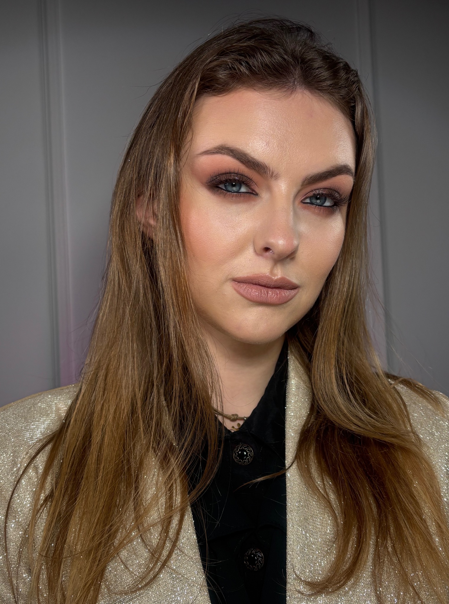 Portret kobiety z subtelnym, wieczorowym make-up'em: brązowe cienie, podkreślone oczy, nude usta. Uwagę przyciąga złota marynarka z połyskującymi drobinkami.