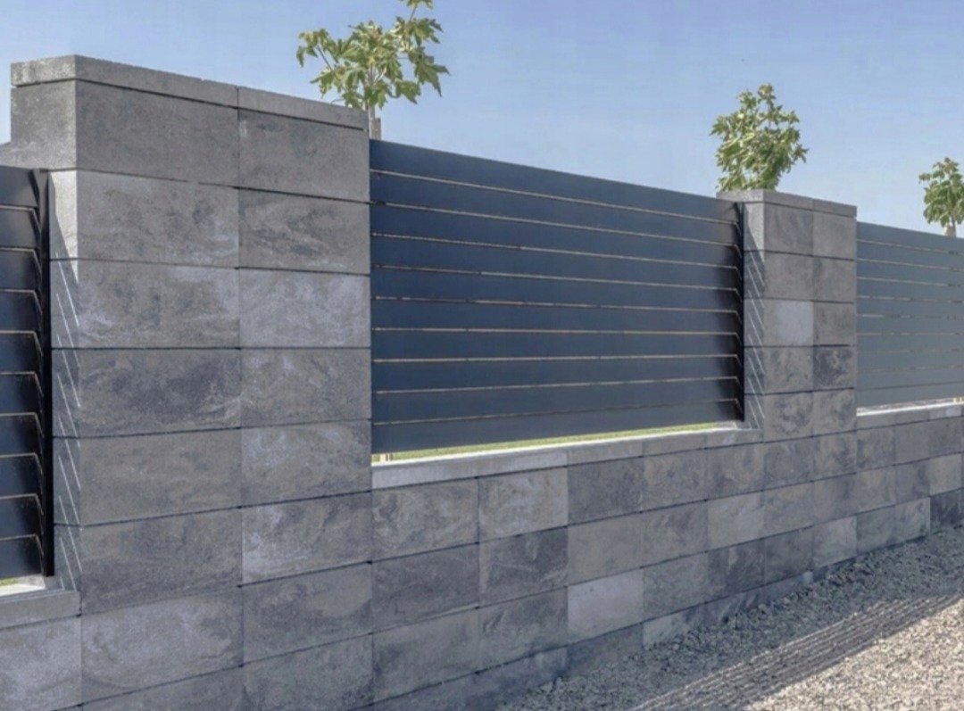 Nowoczesne ogrodzenie z szarego kamienia łupanego i poziomych, metalowych paneli. Minimalistyczny design z młodymi drzewkami w tle.