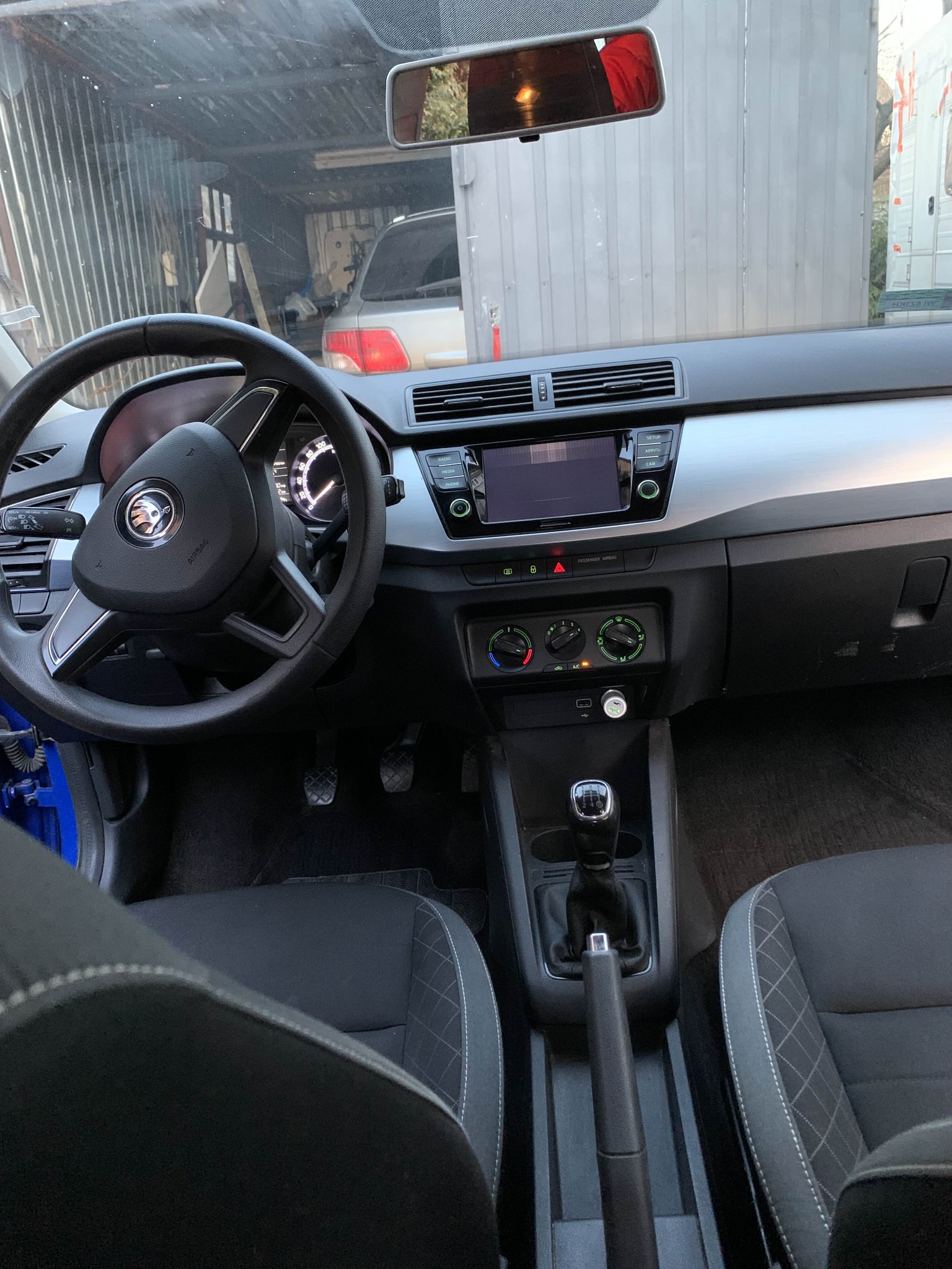 Wnętrze samochodu Skoda Fabia z manualną skrzynią biegów. Widoczna deska rozdzielcza, kierownica z logo marki oraz fragmenty foteli z jasnymi przeszyciami.