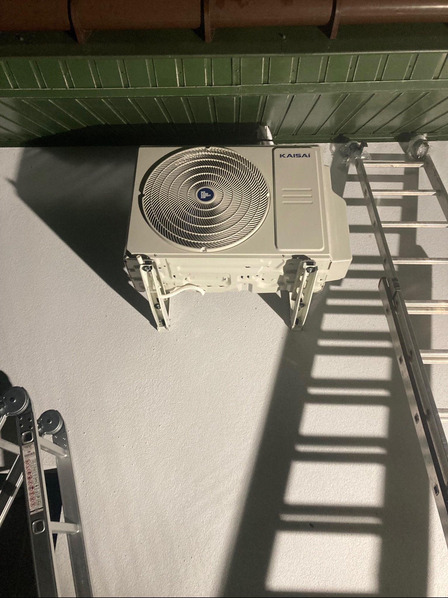 Montaż klimatyzacji Kaisai w Siekierczynie. Widoczna jednostka zewnętrzna na elewacji budynku, drabina oparta o ścianę. Urządzenie gotowe do podłączenia.