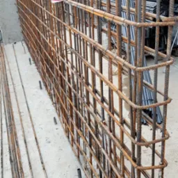 Siatka zbrojeniowa ze stalowych prętów, przygotowana do zalania betonem, widoczna z bliska, z detalami wiązań i prętów wystających z posadzki.