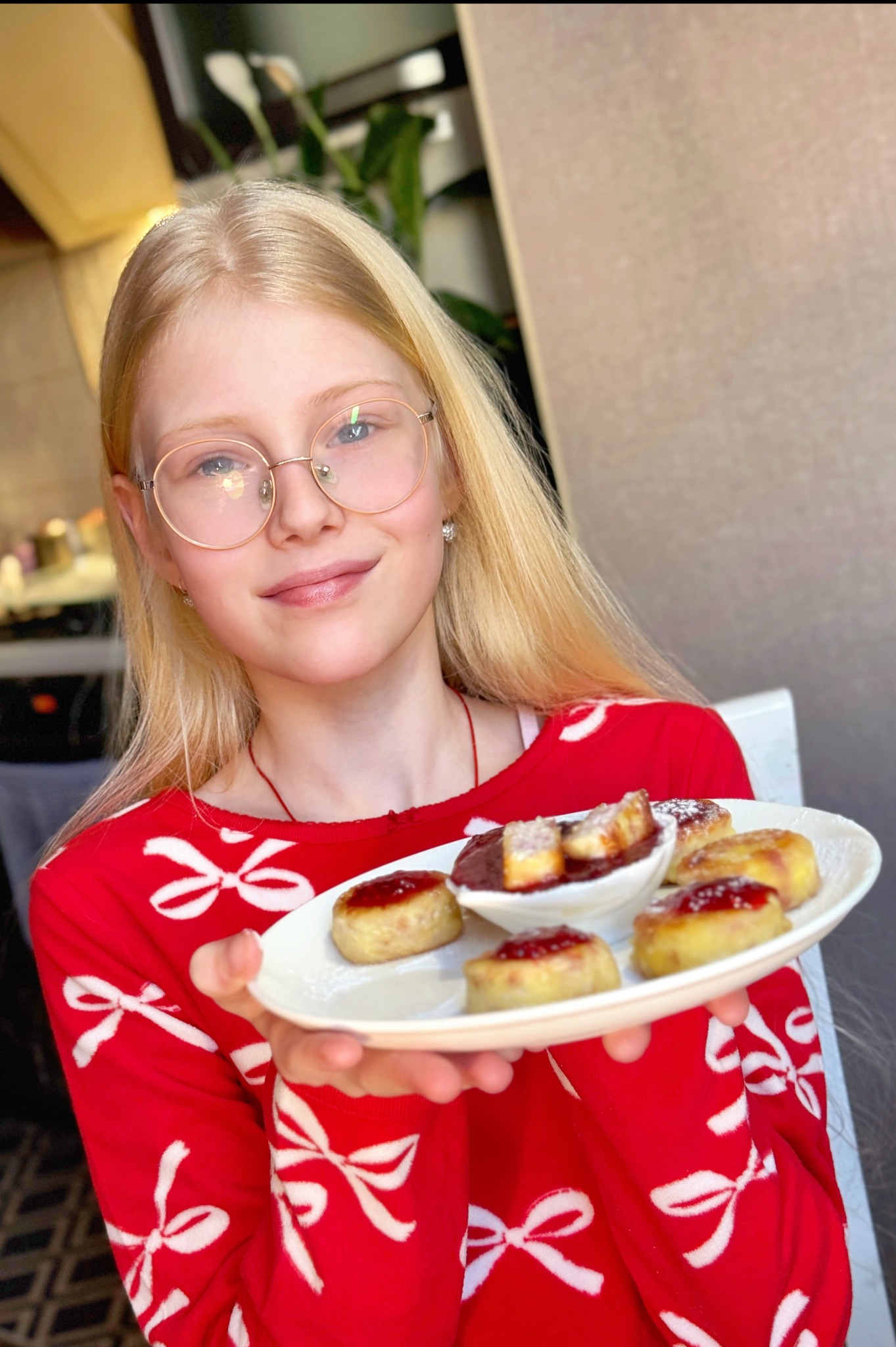 Uśmiechnięta dziewczyna w czerwonej bluzce prezentuje talerz z mini serniczkami z dżemem i sosem w białej miseczce, idealne na słodki catering.