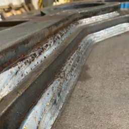 Metalowa konstrukcja po spawaniu, widoczne spoiny i obróbka krawędzi. Szlifowana powierzchnia z widocznymi detalami procesu.