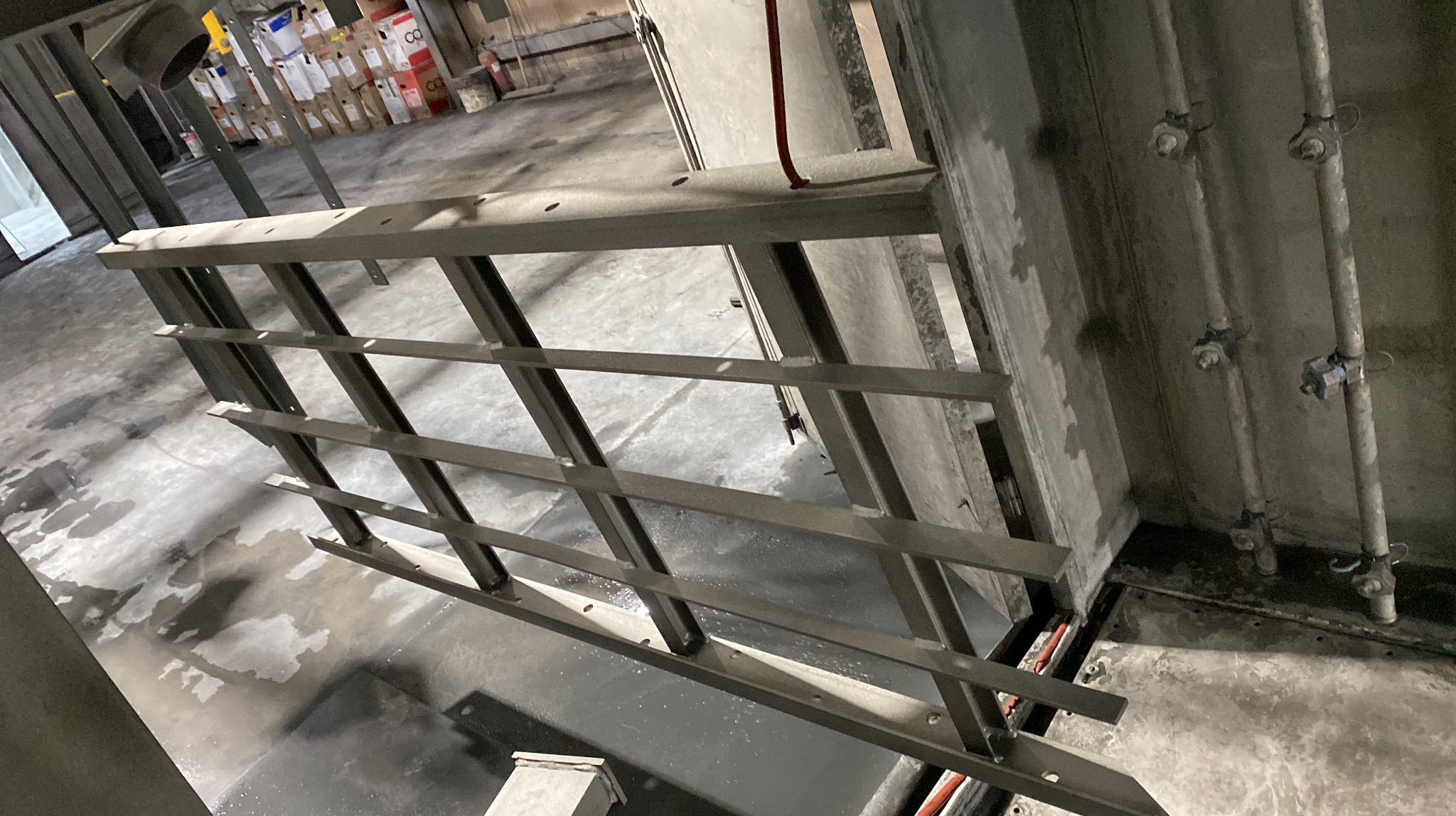 Surowa, stalowa balustrada z prostokątnych profili, w trakcie montażu w industrialnym wnętrzu. Widoczne ślady po spawaniu i surowy beton.